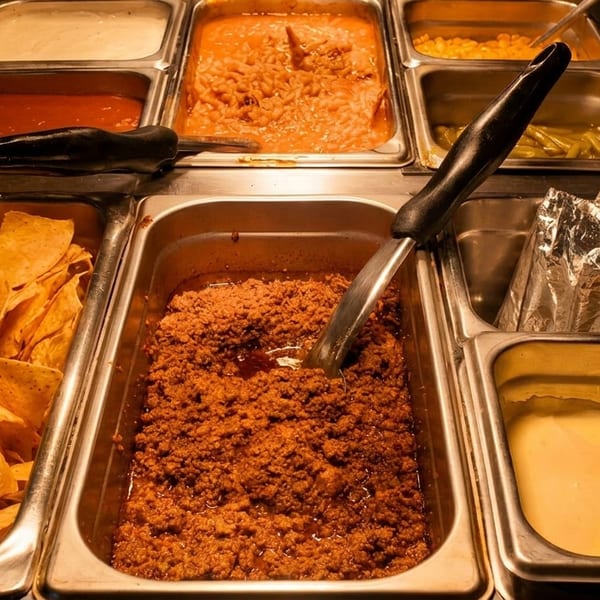 A buffet bar with various Mexican food items including nachos, ground beef, beans, and sauces.