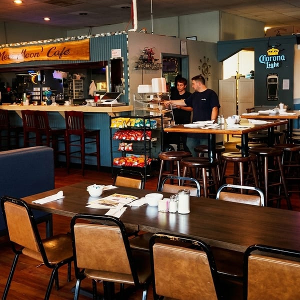 A diner interior with tables, booths, a bar, and two employees behind a snack display.